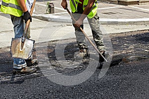 Workers using asphalt paver tools during road construction.