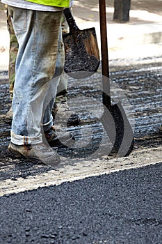 Workers using asphalt paver tools during road construction.