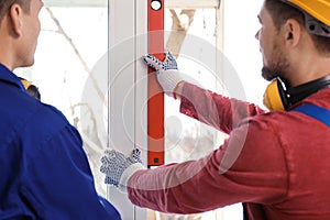 Workers using bubble level for installing window, closeup