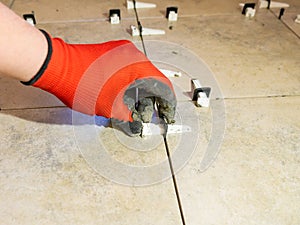 Workers are using plastic clamps and wedges to leveling the ceramic tile on the floor. Tile leveling system.