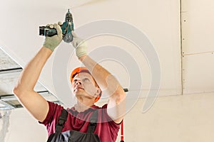 Workers are using screws and a screwdriver to attach plasterboard to the ceiling