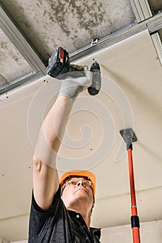 Workers are using screws and a screwdriver to attach plasterboard to the ceiling