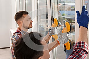 Workers using suction lifters during plastic window installation indoors photo