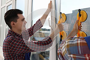 Workers using suction lifters during plastic window installation indoors photo