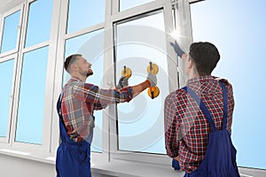 Workers using suction lifters during plastic window installation indoors photo