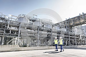 Workers walking past process tanks in oil blending factory.