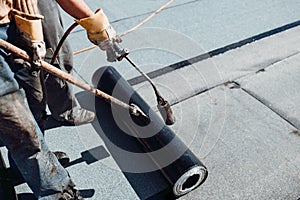 Workers waterproofing flat concrete roof using blowtorch and bituminous membrane rolls