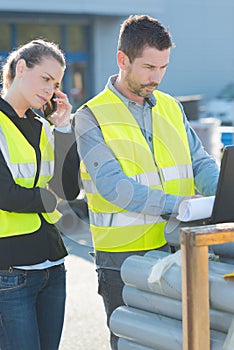 workers wearing high-visibility vests using laptop and smartphone outdoors