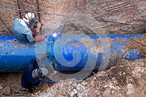 Workers weld large pipes plumbing water system underground at construction site