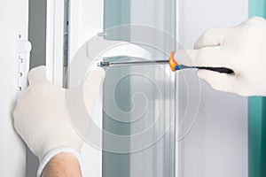 Workerâ€™s hands in protective gloves, screw the handle with a screwdriver to the plastic window, close-up