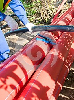 The workerâ€™s hands in white gloves, hold a plastic pipe for cutting with scissors, against the background of red communications