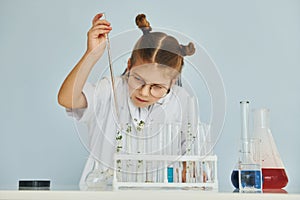 Workes with liquid that is in test tubes. Little girl in coat playing a scientist in lab by using equipment