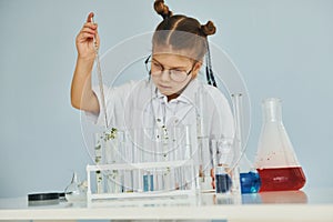 Workes with liquid that is in test tubes. Little girl in coat playing a scientist in lab by using equipment