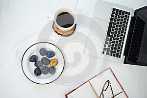 Working in bed , laptop and cup of coffee on white bed