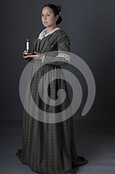 A working class Victorian woman holding a candle in the dark against a grey studio backdrop