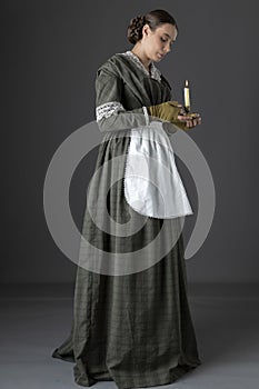 A working class Victorian woman wearing a dark green check bodice and skirt with an apron and holding a candle. photo