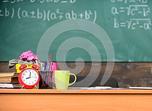 Working conditions which prospective teachers must consider. Table with school supplies alarm clock books and mug