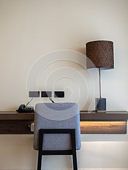 Working corner, back view of empty grey cozy fabric chair seat, black telephone, desk lamp and sockets decorated on wood shelf.