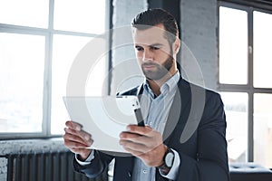 Working day...Serious bearded businessman in stylish suit and with branded watch on his hand is looking at digital