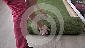 Working decorator unwinds canvas artificial lawn lying on the floor. Close-up of the hands and feet of the worker.