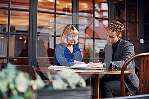 Working with documents. Young guy in formal clothes have a business talk with old woman in cafe