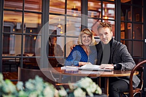 Working with documents. Young guy in formal clothes have a business talk with old woman in cafe