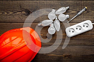 Working with electrical equipment. Hard hat, socket outlet, bulbs, screwdriver on dark wooden background top view copy