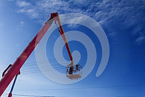 Working electrician working at height on hydraulic aerial platform against the blue sky.