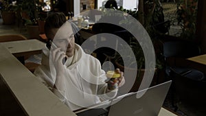 Working environment. Stock footage. A young man sitting in a cafe and working at a laptop while talking on the phone.