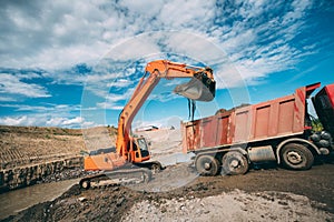 Working excavator on site, loading dumper truck during earthmoving works photo