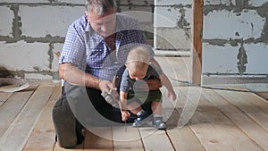Working fun grandfather and grandson on the construction site. Grandfather teaches his grandson the baby to hammer nails