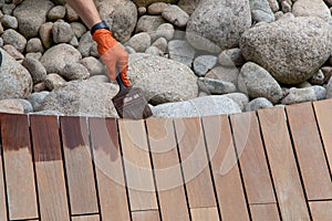 Working hand applying wood deck oil on hardwood boards