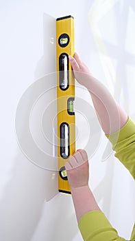 Working hands check evenness of wall with special tool for measuring level