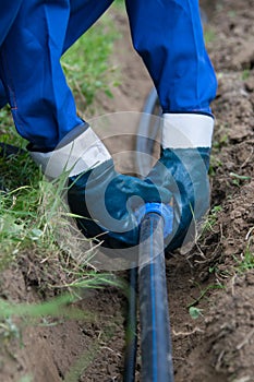 The working hands in gloves, put the plastic pipe in the dug trench in the ground