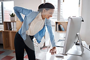 Working hard has its downsides. a young businesswoman experiencing back pain while working at her desk in a modern