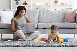 Working From Home. Freelancer Lady Using Laptop And Smartphone While Babysitting Child