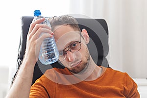 Working at home man suffering from heat and thirst cools down with water bottle at hot summer day