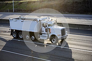 Working horse big rig tipper truck with two trailers running on the highway road with sun light