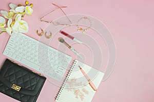 Working items for women with keyboard, flowers, bag and notebook over the pink background.