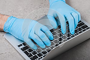 Working at a laptop in blue medical gloves. Protect your hands from bacteria and viruses when working on a laptop in public places