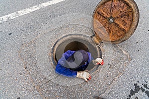Working man comes out from the Sewerage hatch in the ground on city street