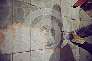 A working man with a drill puncher disassembles an old tile from a concrete wall
