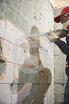 A working man with a hammer drill disassembles an old tile from a concrete wall