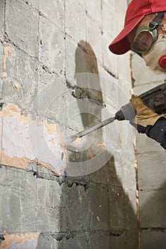 A working man with a hammer drill disassembles an old tile from a concrete wall