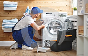 Working man plumber repairs washing machine in laundry