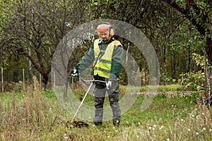 A working man in professional outfit mows grass with a trimmer, a mower. Mowing lawns, roadsides, edge