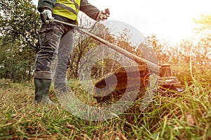 A working man in professional outfit mows grass with a trimmer, a mower. Mowing lawns, roadsides, edge photo
