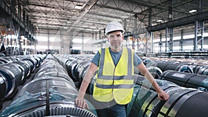 A working man in a rolled metal warehouse. A man in overalls and a protective helmet.