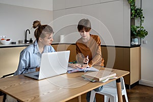 Working mom doing job on laptop and homework with son on kitchen at home.