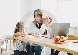 Working mom freelancer on laptop with little daughter drawing on the table at home